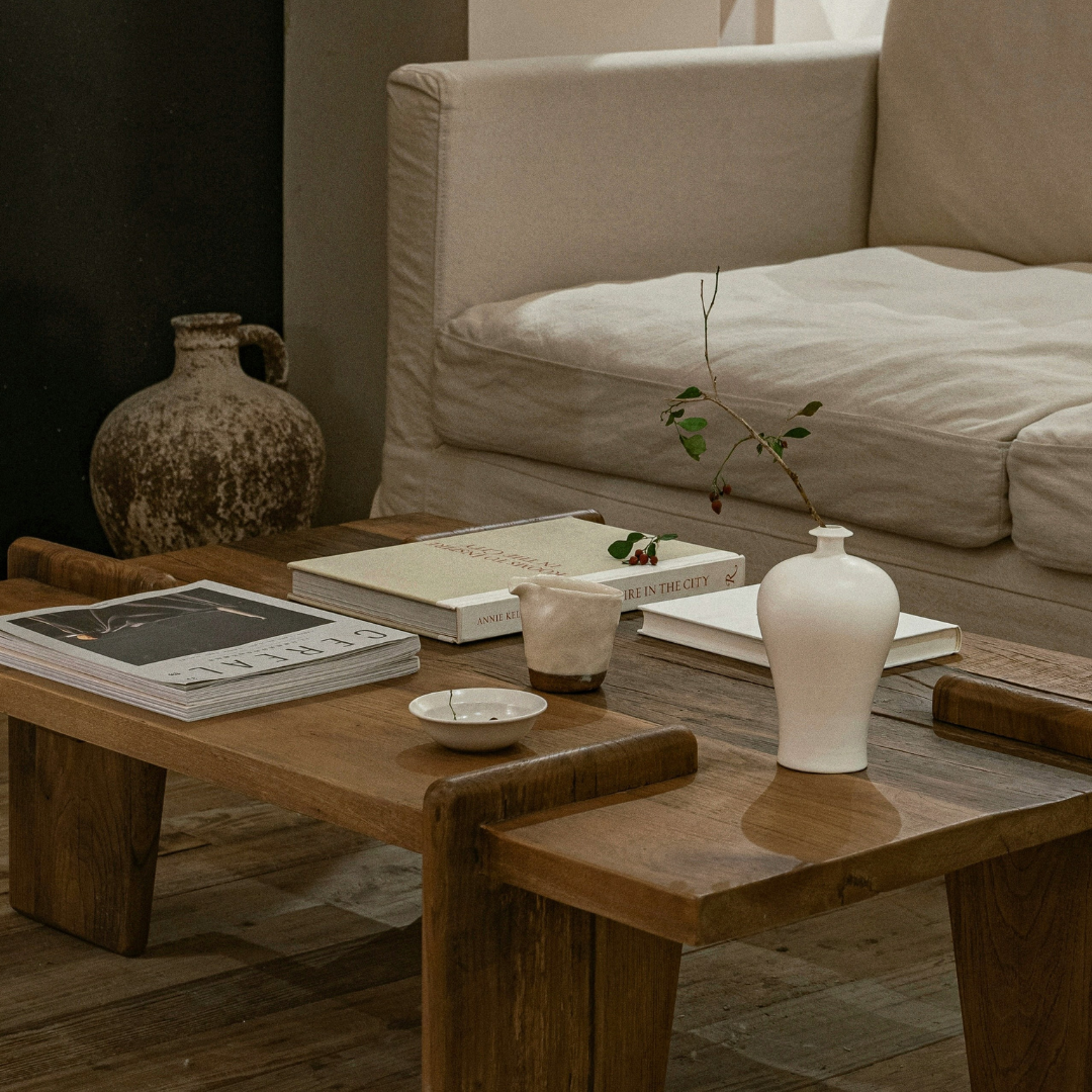 Curated fragrance gifts on rustic coffee table with white vase, candle, books and modern sofa