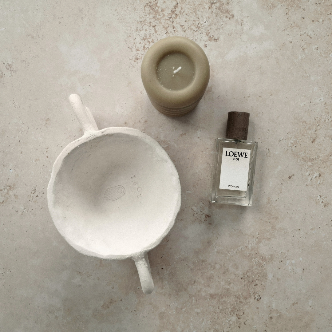 Minimalist flatlay with a beige candle, Loewe perfume, and handmade ceramic bowl on stone