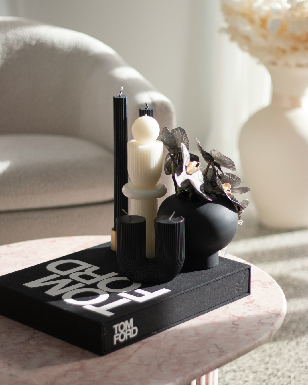 Modern black and white candles and vase on Tom Ford book, styled on a marble table in sunlight