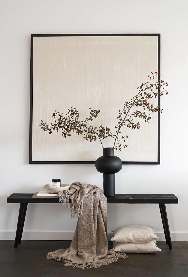 Minimalist home decor with a black vase, autumn branches, candle, throw blanket, and neutral art