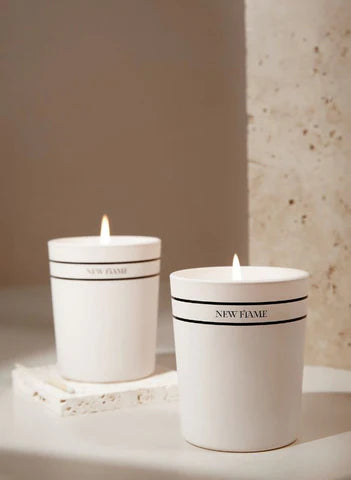 Two white scented candles labeled 'New Flame' on a minimal stone surface, Moodie Saunter gifts.