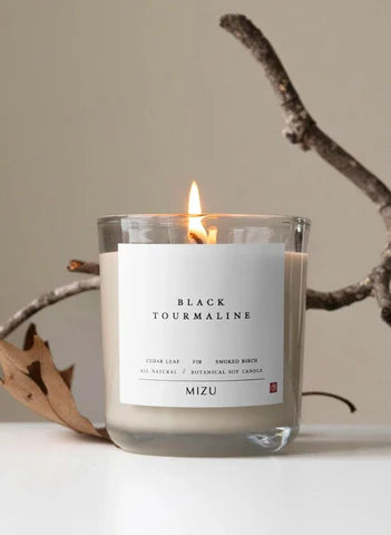 Black Tourmaline scented candle by Mizu lit on neutral background with branch, Moodie Saunter